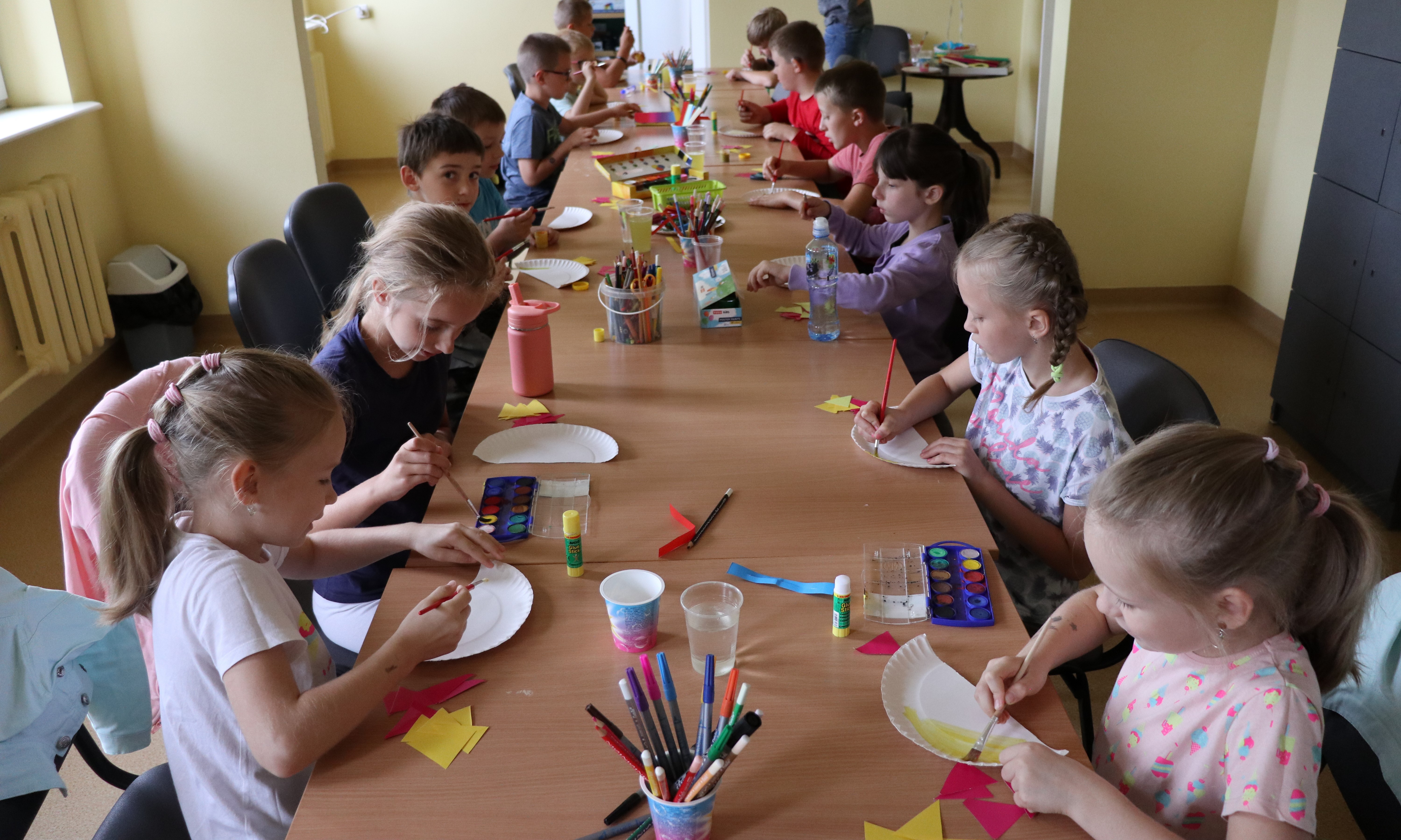 Grupa dzieci tworzy prace plastyczne z papierowych talerzyków. 